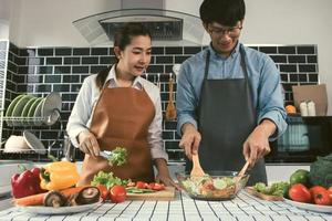 pareja asiática disfrutando de cocinar ensalada de verduras en la cocina.