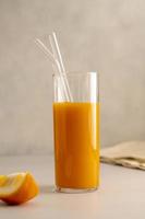 Orange juice glass with reusable glass straws, on bright background