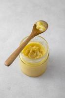 Ghee in a glass jar made with sunflower oil on a light background, copy space for text. Hard light. photo