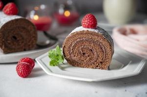 Chocolate roll cake or swiss dessert cake with raspberries. Romantic mood with candles.