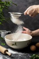 Woman's hand sifting flour through sieve. Selective focus. Baking, cooking, pastry abstract concept. Dark background