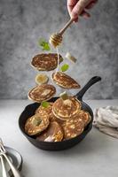 Levitating pancakes in frying, skillet pan with honey,banana, butter and mint leaves, breakfast