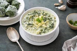 Creamed spinach with cheese in white bowl on dark background. Healthy food photo