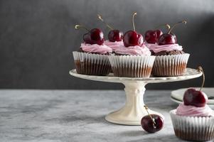 Chocolate cupcakes with fresh cherries and pink cream on cake stand. Beautiful dessert. Dark background.