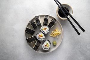 sushi en plato redondo con palillos, salsa de soja. jengibre. rollos caseros con salmón, aguacate y pepino.