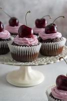 Chocolate cupcakes with fresh cherries and pink cream on cake stand. photo
