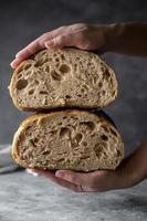 Female hands holding sourdough artisan homemade bread sliced in halfs, dark background. photo