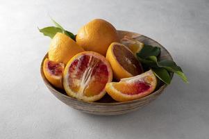 Bloody oranges in wooden bowl, on bright background, whole and slices with leaves fresh citrus fruits photo