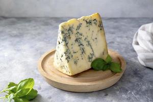 Blue cheese, dor blue or roquefort mold cheese slice on cutting board with basil leaves, lifestyle food.