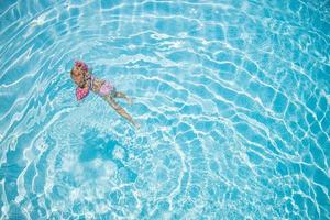 linda niña pequeña nadando en una piscina turquesa con brazos inflables, ayuda para apoyar, vista superior. foto