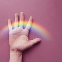 mano con un arco iris en la pared rosa. simbolo LGBT foto