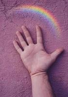 mano con un arco iris en la pared rosa. simbolo LGBT foto