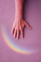 mano con un arco iris en la pared rosa. simbolo LGBT foto