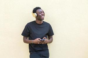 Delighted young black man listening to song in headphones and surfing smartphone photo