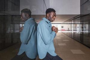 Unhappy young black man standing in passage near glass wall photo