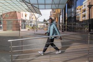 genial chico afroamericano caminando cerca de un edificio contemporáneo y mirando hacia otro lado foto