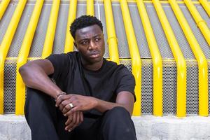 Dreamy young African American male sitting on street and looking away photo