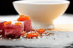 Tuna sashimi dipped in soy sauce with salmon roe, thick salt and dill on slate stone with bowl with soy. Raw fish in traditional Japanese style. Horizontal image. photo