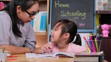 asiatisk liten flicka studerar hemma under karantän med sin mamma. mamma hjälper lilla dotter med läxor hemma. hemundervisning. video