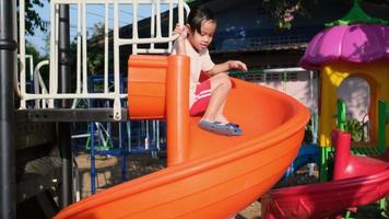 niña activa en el patio de recreo al aire libre. linda niña deslizándose hacia abajo en el control deslizante. Actividad de verano saludable para niños. video