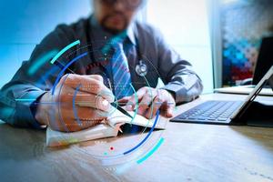 medical doctor writing on notebook and digital tablet docking keyboard with laptop on marble desk,sun flare effect photo