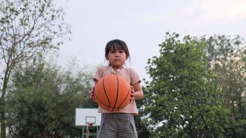 fröhliches süßes Mädchen, das draußen Basketball spielt. video
