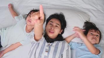 Draufsichtporträt von glücklichen Kindern, die mit ihrer Mutter spielen, die zu Hause auf einem Bett liegt und in die Kamera schaut. schöne Zeit zu Hause. video