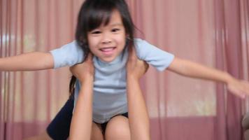 Happy children playing with mom at home. Mother lies on the warm floor and lifts up her little daughter, imagining herself as an airplane enjoying flying in the air. video