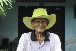 un retrato de un viejo granjero indonesio usa un sombrero amarillo con una bicicleta vieja foto