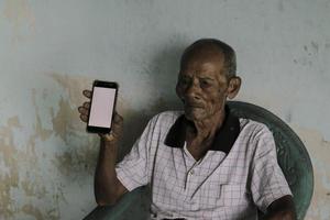 A portrait of Indonesian old grandpa showing white screen smartphone. photo