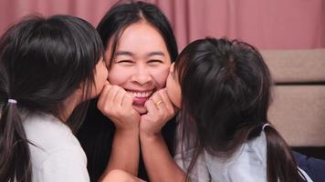 Two tender daughters kissing happy mother. Happy children playing with their mother lying on a bed at home and  looking at the camera. video