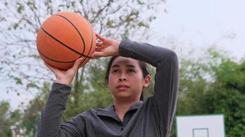 atleta feminina asiática usando poses de fones de ouvido com basquete na quadra de basquete ao ar livre.