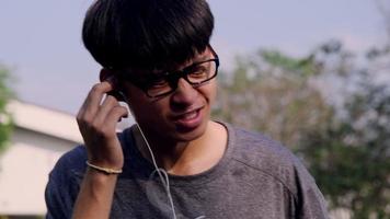 feliz jovem asiático usando fone de ouvido ouvindo música no jardim de verão. video