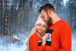 beautiful couple standing arm in arm in the red sweater in the background of the forest in winter , a walk in the winter woods photo