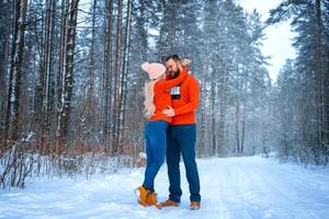 beautiful couple standing arm in arm in the red sweater in the background of the forest in winter , a walk in the winter woods photo