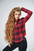 A beautiful young woman with beautiful long hair poses on a white background in a red checked shirt photo