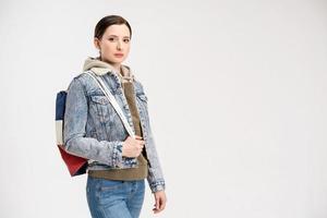 linda mujer joven en una chaqueta de denim y con una mochila posando sobre un fondo blanco foto