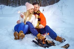 Happy couple in winter in the forest by the fire with sparklers photo