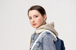 linda mujer joven en una chaqueta de denim y con una mochila posando sobre un fondo blanco foto