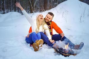 happy couple man and woman in winter in the forest fry marshmallows on the fire photo