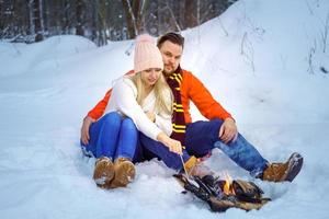 happy couple man and woman in winter in the forest fry marshmallows on the fire photo