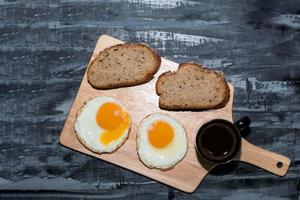 la comida del desayuno rebanada de pan de huevo frito tiene café expreso en la tabla de cortar. foto