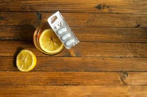 Top view, a cup of tea with lemon and cold pills on wooden background. photo