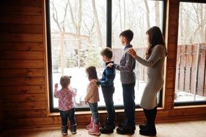 Mother and four kids in modern wooden house against large window. photo