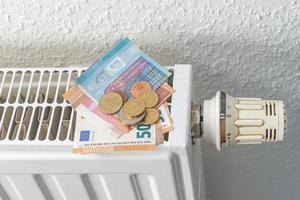 House heating battery with maximum heating power setting dial and a pile of money banknotes and coins in euro. Concept of energy consumption, energy crisis in households.