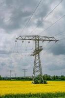 hermoso paisaje agrícola con colza amarilla en el campo de flores, turbinas eólicas para producir energía verde y líneas eléctricas de alto voltaje en alemania, en primavera y cielo lluvioso dramático. foto