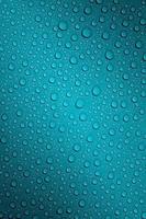 Wet with water drops dark turquoise background with gradient illumination at two corners, macro photo