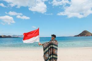 A man with Indonesia traditional fabric called Kain Songket waving Indonesian flag on the beach photo
