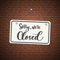 Sorry, we are closed. White sign with shadow isolated on red brick background.