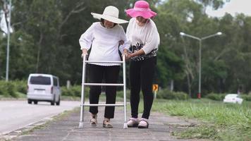Daughter take care elderly woman walking on street in strong sunlight. video